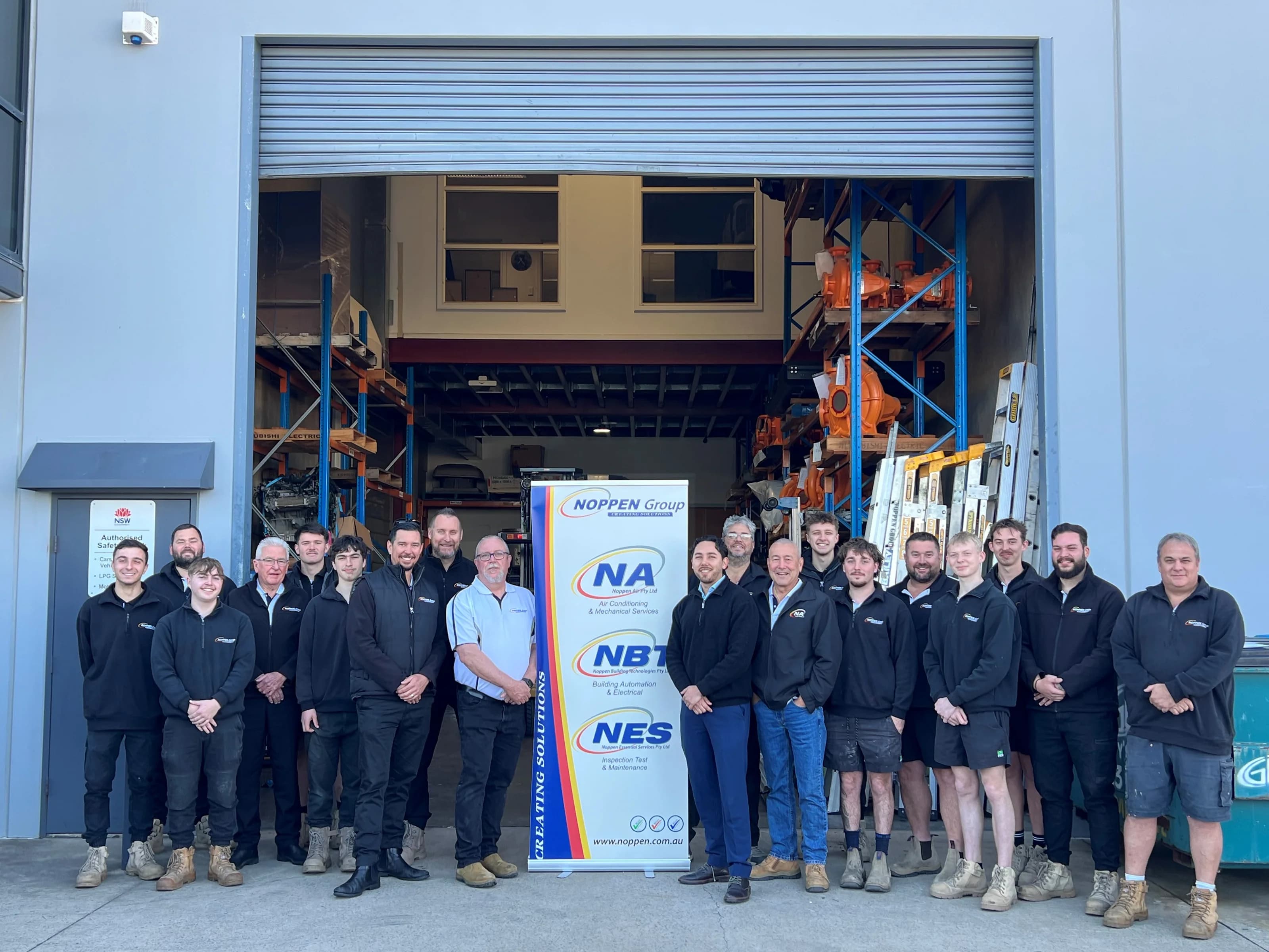 The Noppen Group team standing together in front of the Noppen warehouse beside a Noppen Group banner